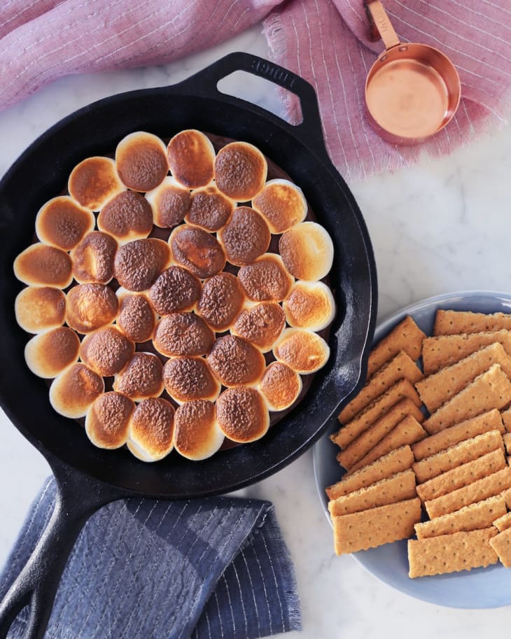 Marshmallows, with a crusty edge on top, on a cast iron skillet with a plate of crackers on the side