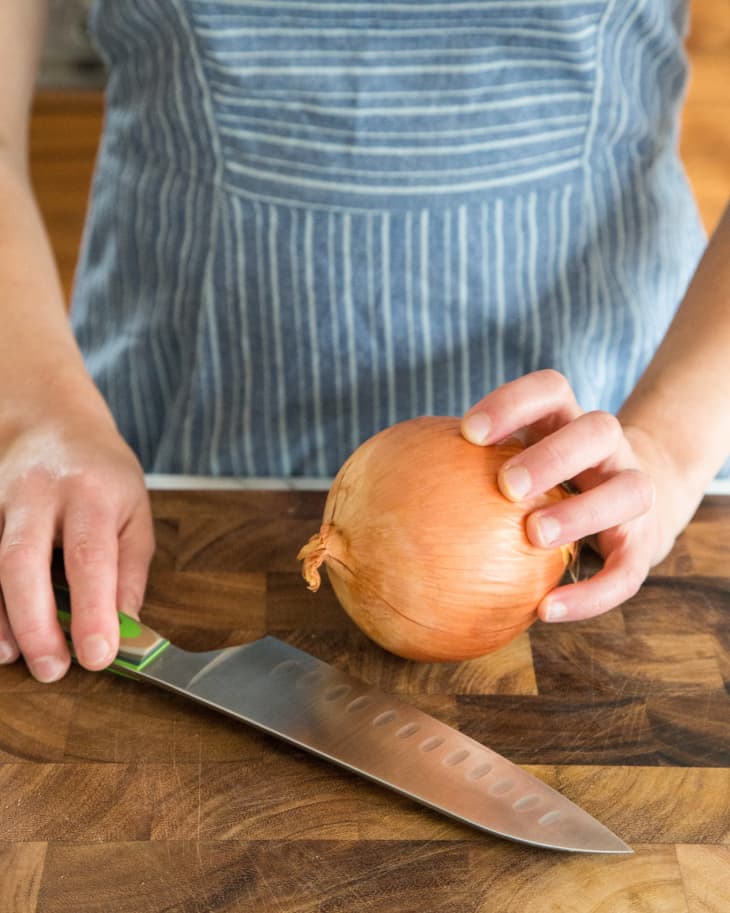 Woman in blue apron about to chop up a yellow onion