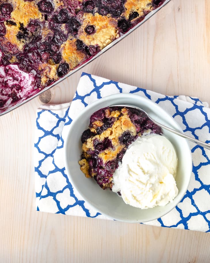 Blueberry Dump Cake baking dish, bowl with one piece cut out with vanilla ice cream