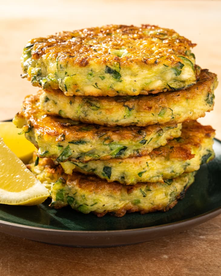 stack of zucchini pancakes on plate with lemon wedges