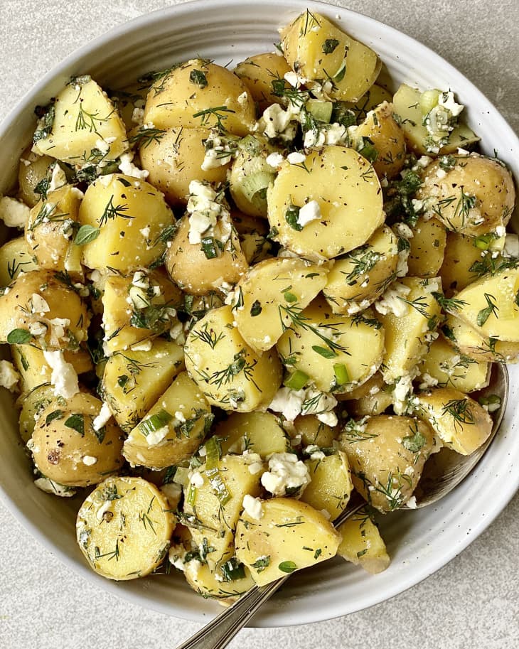 bowl of potatoes, potato chunks, dill, feta cheese crumbles, silver spoon