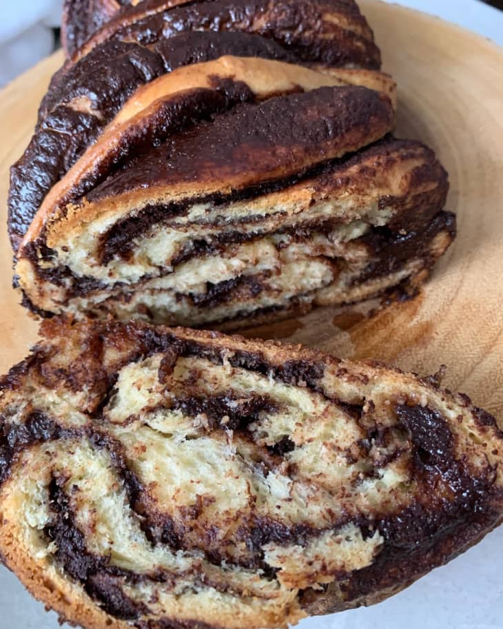 Sliced chocolate babka on a wooden board, showing swirled layers of chocolate and dough.