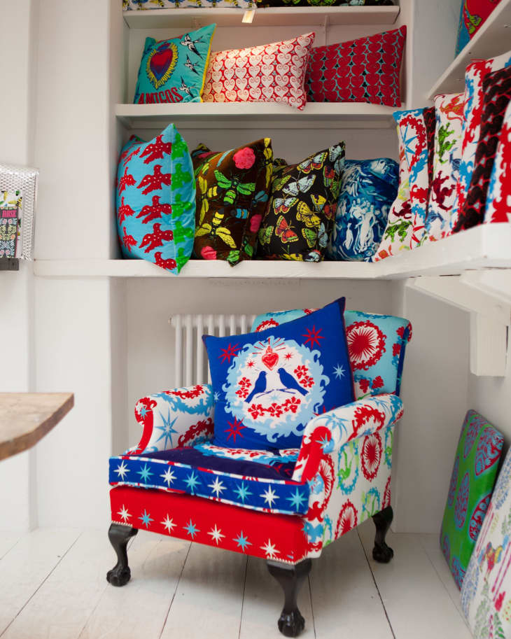 Colorful armchair with star patterns, surrounded by vibrant, patterned cushions on white shelves.
