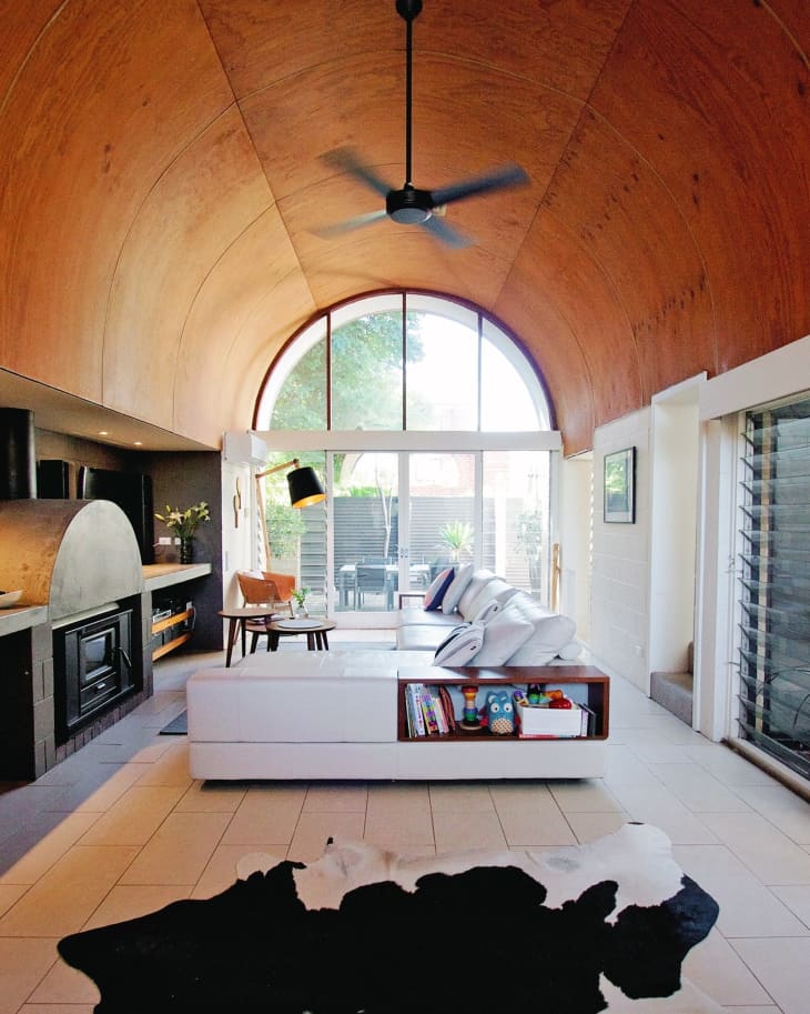 Modern living room with arched wooden ceiling, white sectional sofa, black fireplace, and large window overlooking patio.