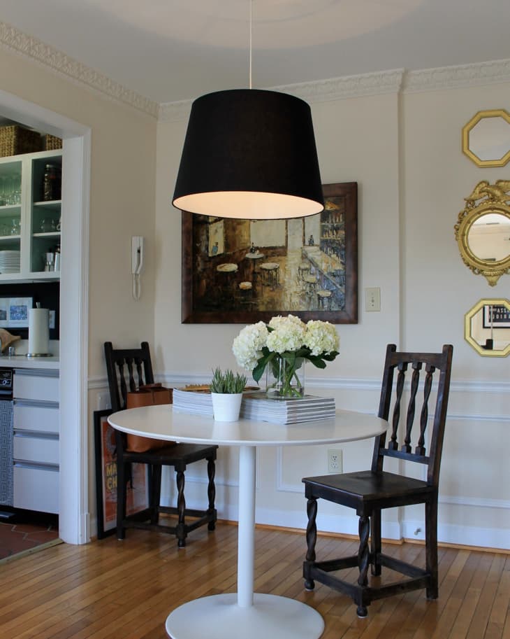 Dining area with round white table, dark wooden chairs, black pendant light, and a vase of white flowers.