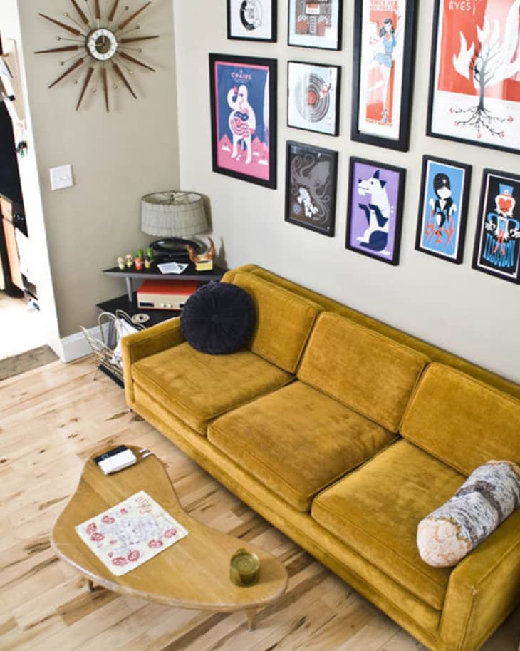 Mid-century modern living room with mustard sofa, starburst clock, and gallery wall of colorful framed art.