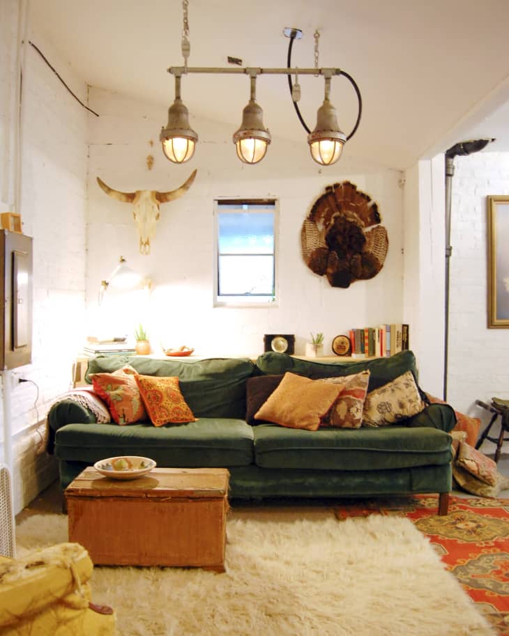 Cozy living room with green sofa, colorful pillows, rustic decor, and industrial pendant lights.