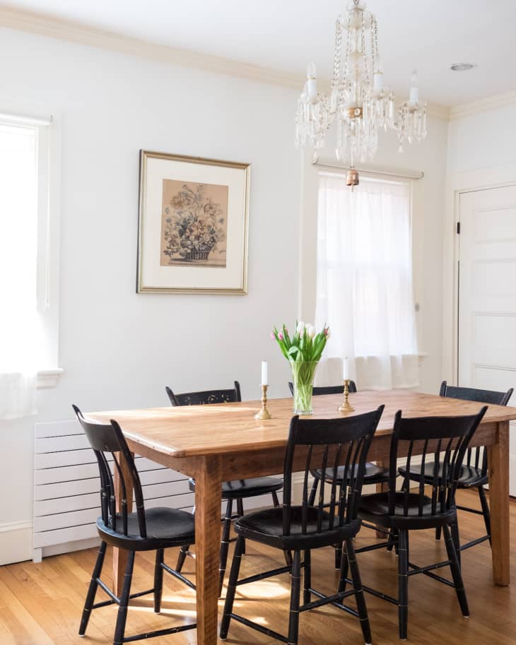 Dining room with wooden table, black chairs, chandelier, framed artwork, and vase of tulips.