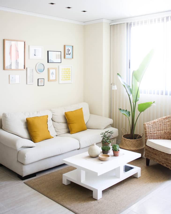 Living room with a white sofa, yellow cushions, white coffee table, potted plants, and a gallery wall.