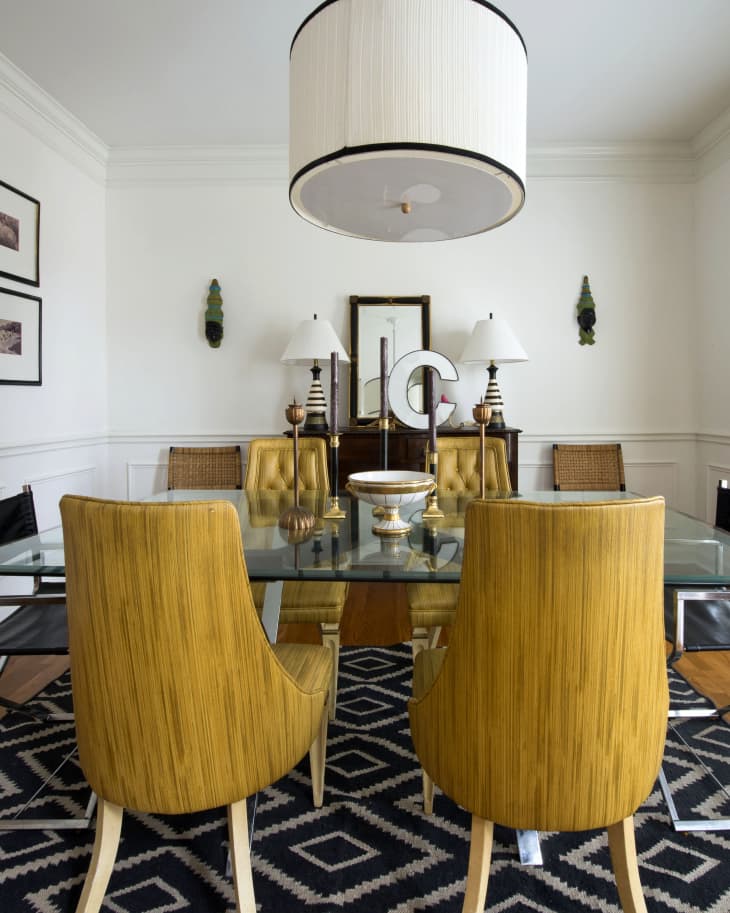Dining room with glass table, yellow chairs, large pendant light, and geometric black and white rug.