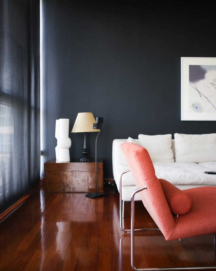 Modern living room with a white sofa, red chair, dark wall, wooden floor, and abstract wall art.