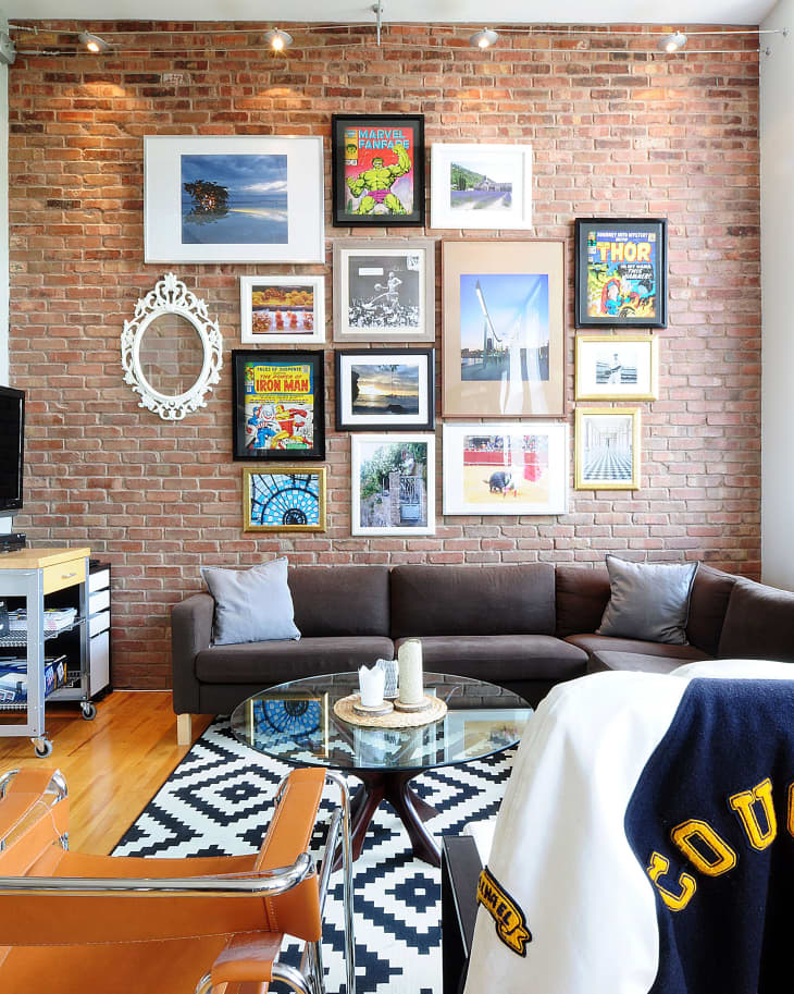 A brick wall with many pictures on it behind a couch.