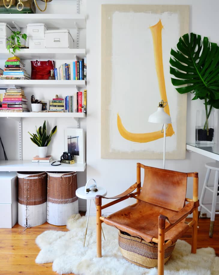 Cozy reading nook with leather chair, white rug, bookshelves, large abstract art, and a potted plant.