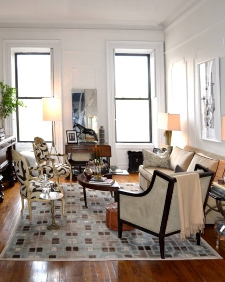 Elegant living room with patterned chairs, a beige sofa, wooden floors, and large windows, featuring modern decor and lamps.
