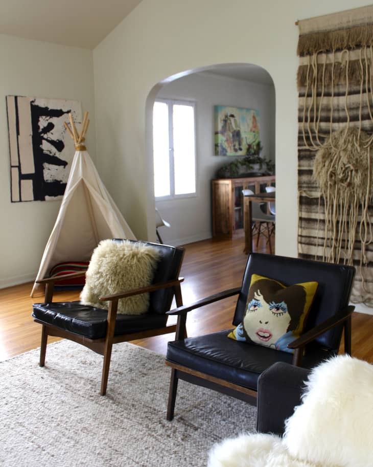 Mid-century modern living room with black leather chairs, a teepee, abstract art, and a woven wall hanging.