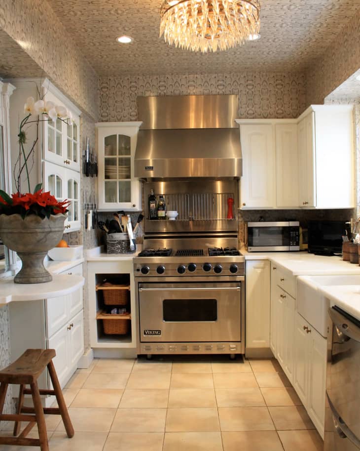 Elegant kitchen with stainless steel Viking stove, white cabinets, crystal chandelier, and decorative wallpaper.