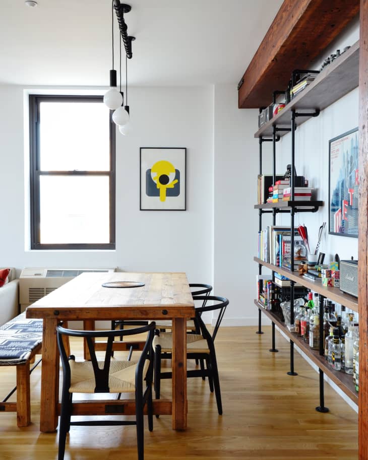 Dining room with wooden table, black chairs, wall art, and shelves filled with books and bottles.