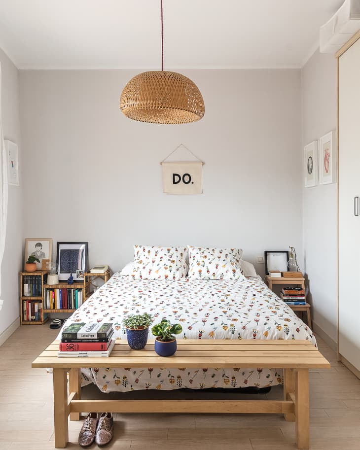 Bedroom with floral bedding, wooden bench, books, potted plants, and a wicker pendant light.