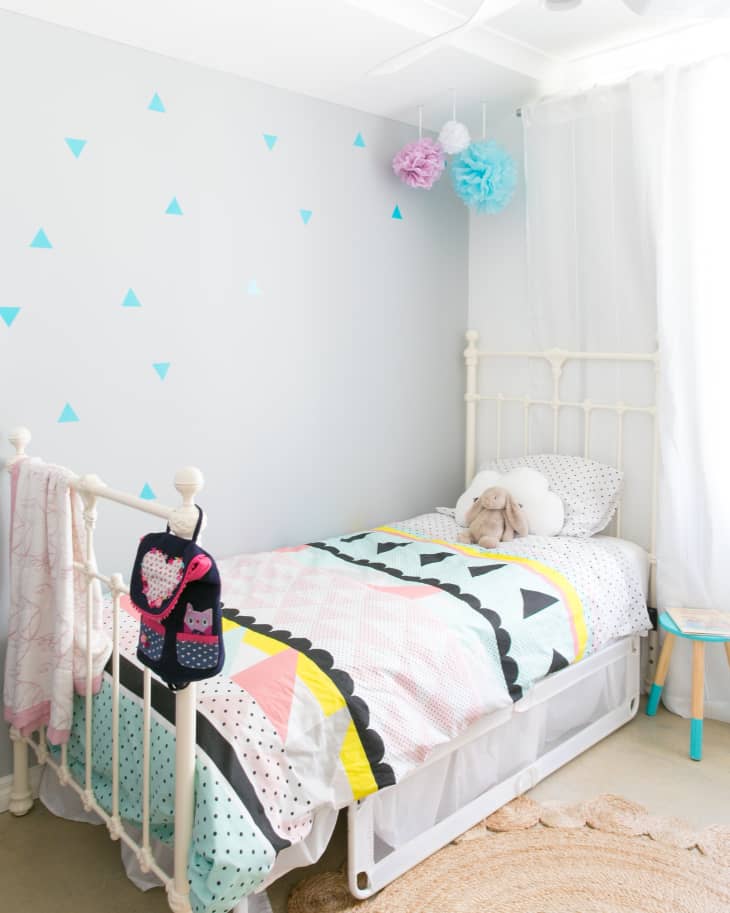 Child's bedroom with a white metal bed, colorful geometric bedding, and hanging pom-poms.