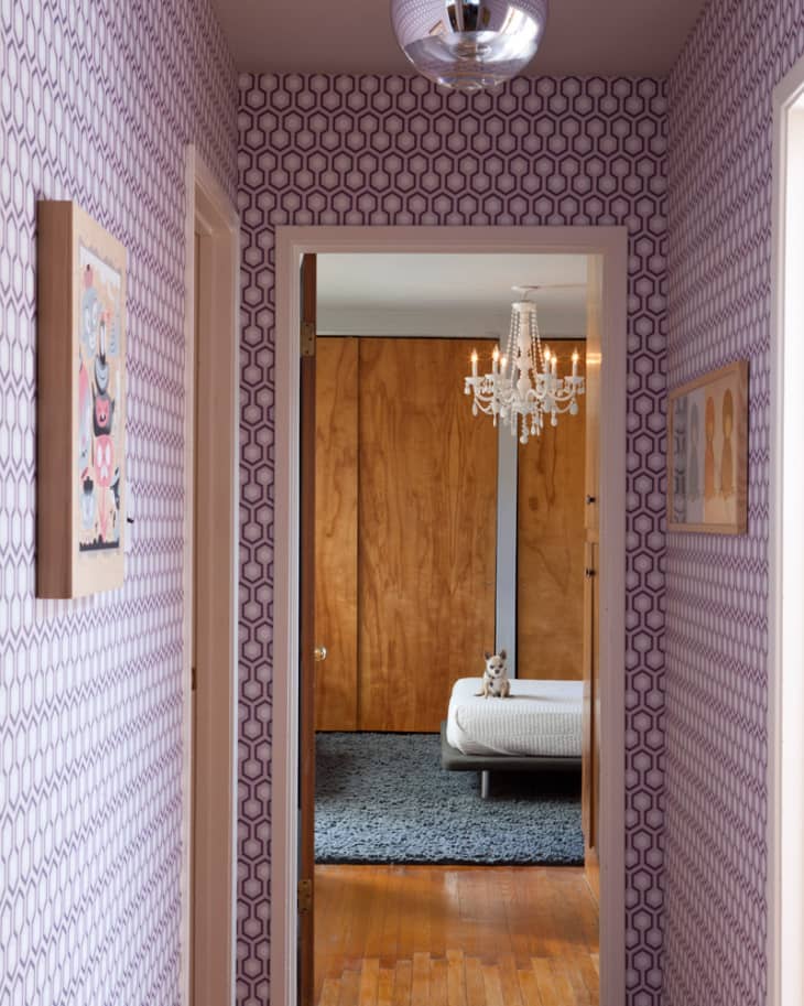 Hallway with geometric wallpaper leading to a bedroom with a chandelier, wooden walls, and a bed with a stuffed animal.