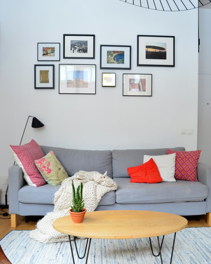 Gray sofa with colorful pillows, gallery wall, wooden coffee table, and potted plant in a cozy living room.
