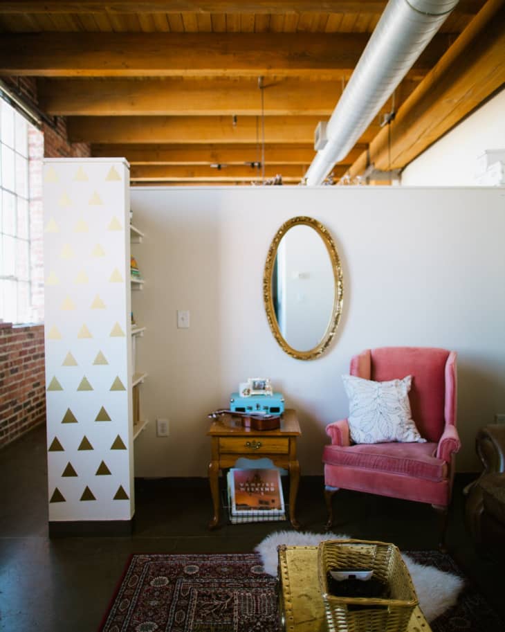 Cozy living area with a pink armchair, gold oval mirror, wooden side table, and a blue record player.