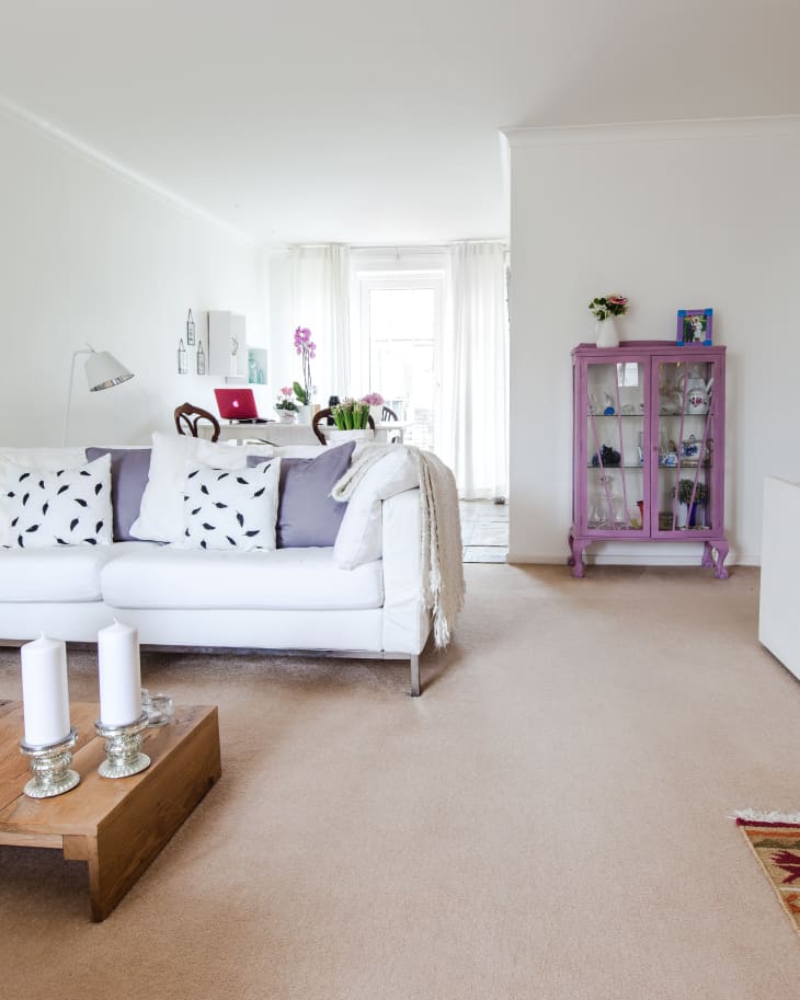 Living room with white sofa, patterned pillows, purple cabinet, and wooden coffee table with candles.