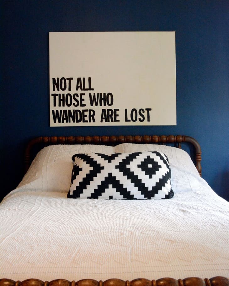 Bed with white quilt, geometric black and white pillow, and wall art saying "Not all those who wander are lost."