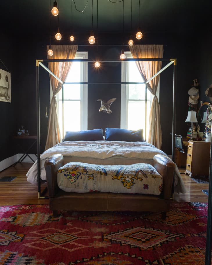 A bed with a metal frame sitting below a Edison light chandelier.
