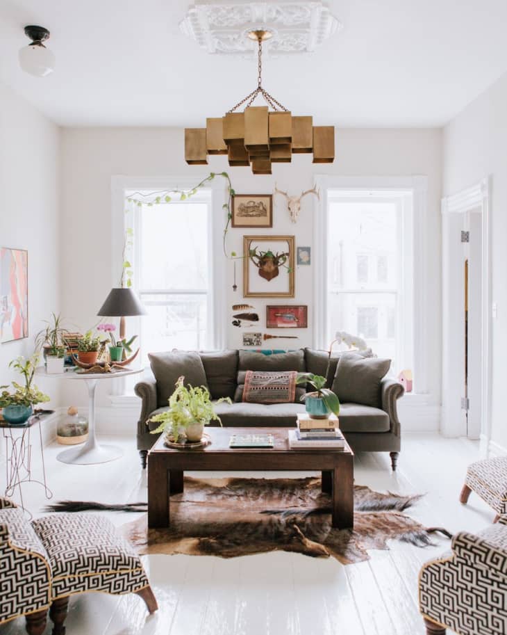 Living room with a gray sofa, patterned chairs, wooden coffee table, plants, and eclectic wall art under a geometric chandelier.