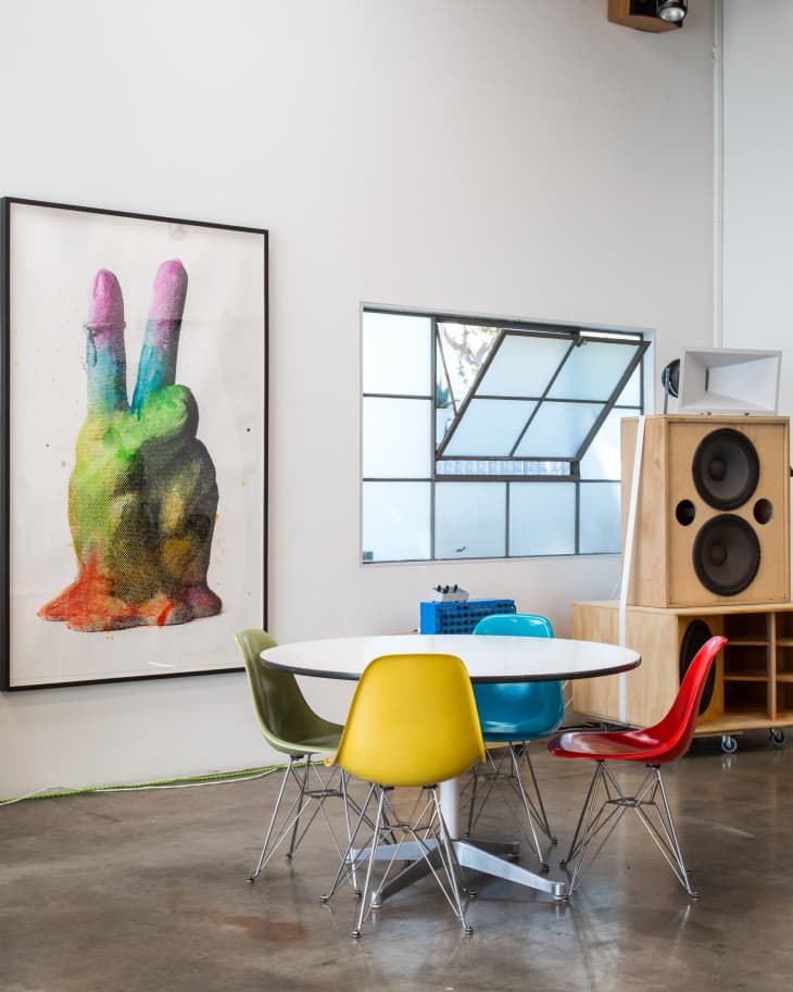 Modern dining area with colorful chairs, round table, large artwork, and speaker system.