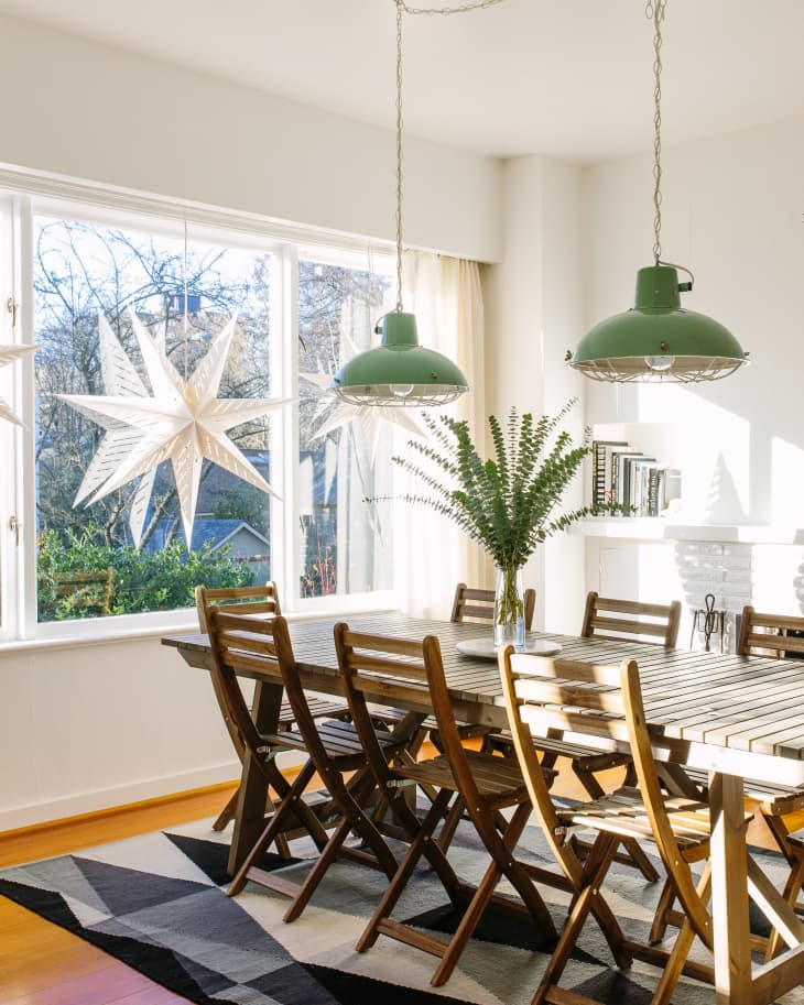 Dining room with wooden table and chairs, green pendant lights, geometric rug, and star-shaped window decorations.