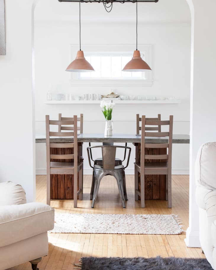 Dining room with wooden table, metal and wooden chairs, pendant lights, and a vase of tulips on the table.