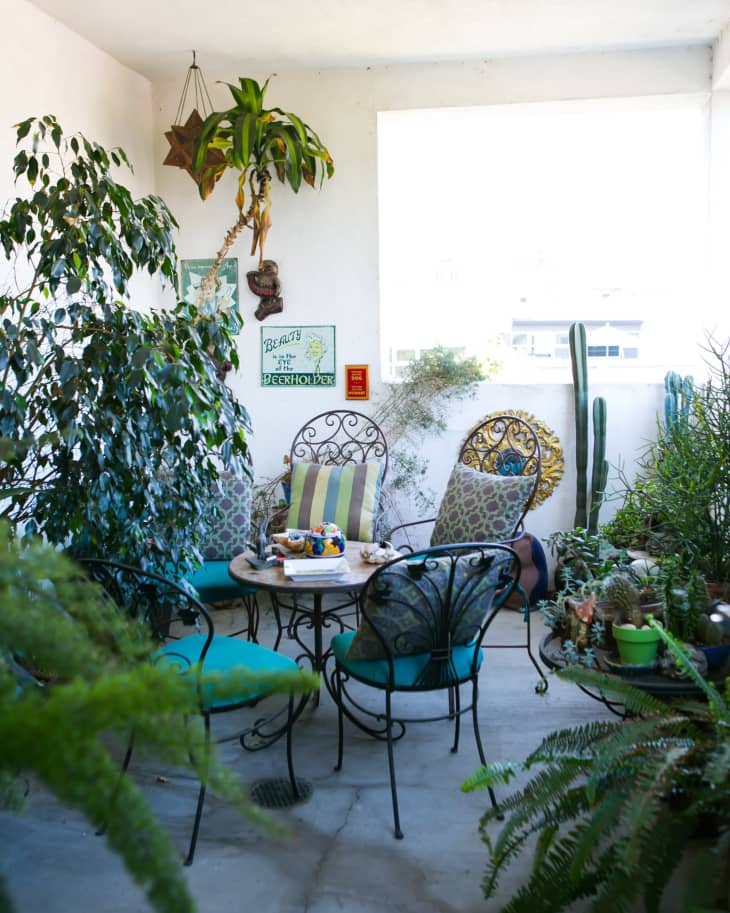 Cozy patio with wrought iron chairs, teal cushions, potted plants, and decorative wall art.
