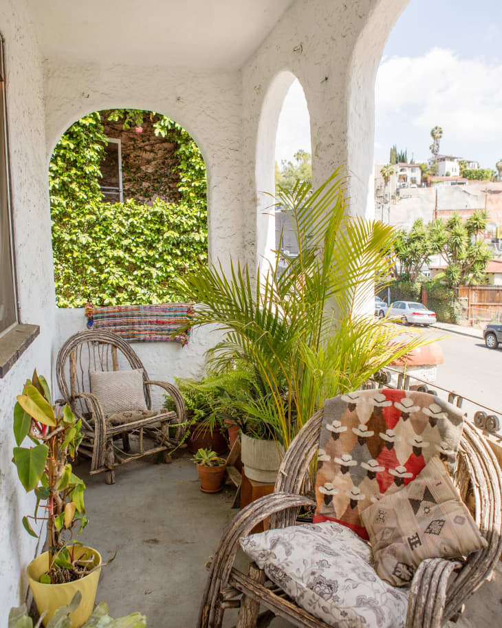 Cozy balcony with wicker chairs, colorful cushions, potted plants, and ivy-covered wall.
