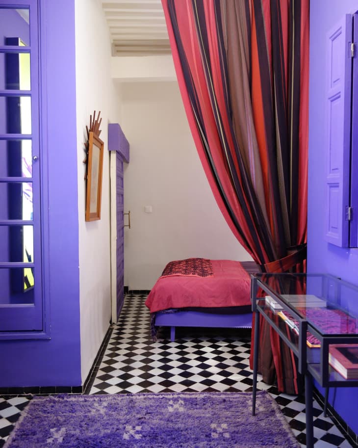 Purple painted walls with a red curtain separating the space between a bedroom and a living area