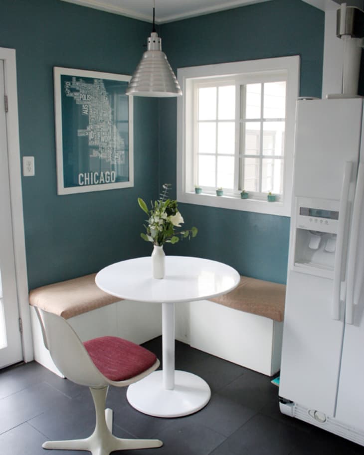 Small kitchen nook with teal walls, white table, red-cushioned chair, and Chicago map art.