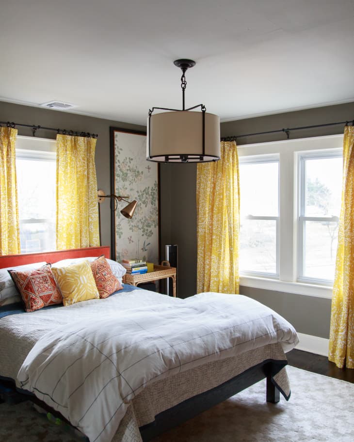 Bedroom with a bed, colorful pillows, yellow floral curtains, and a modern ceiling light.