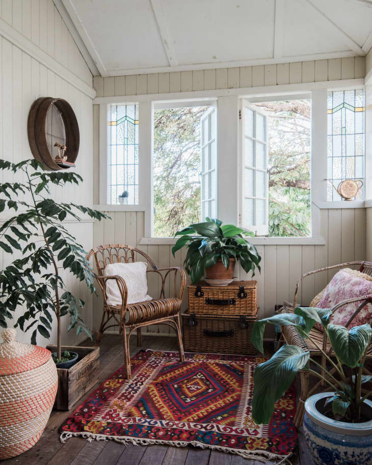 Sunroom with wicker chairs, vibrant patterned rug, potted plants, and open French doors.