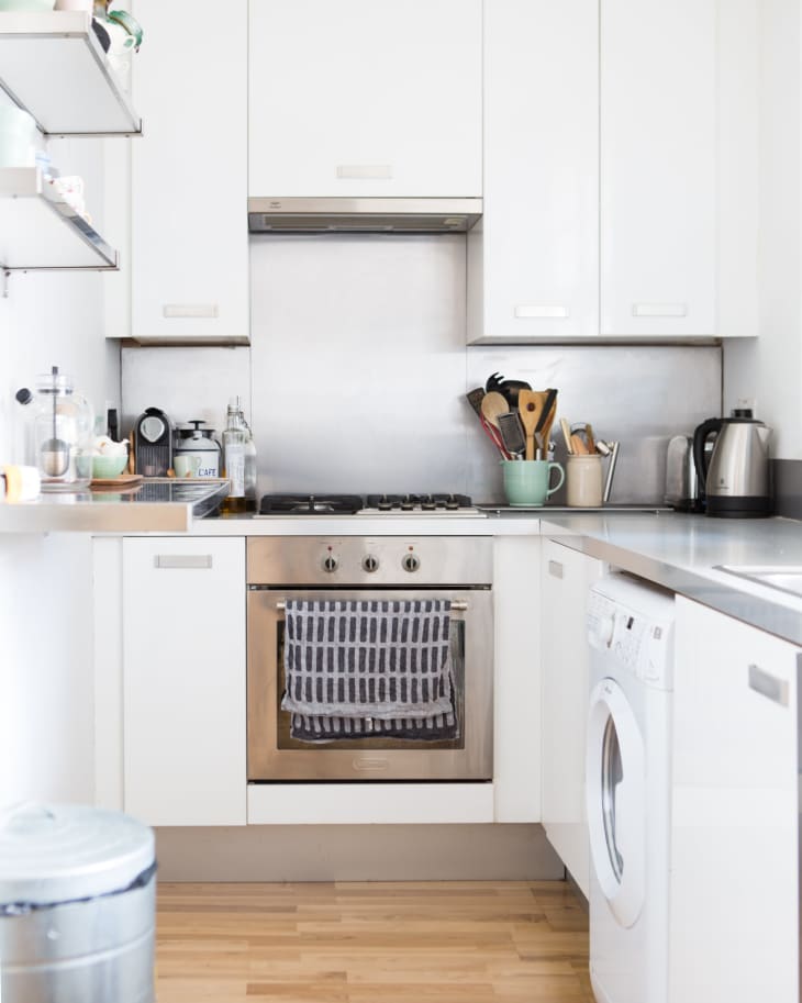 Modern kitchen with white cabinets, stainless steel oven, striped towel, and countertop appliances like a kettle and coffee maker.