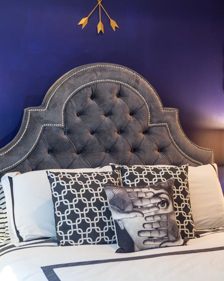 Tufted gray headboard with decorative pillows on a bed, set against a deep blue wall with gold arrow decor.