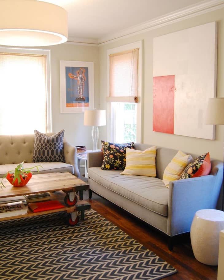 Living room with gray sofas, colorful pillows, wooden coffee table, abstract art, and chevron-patterned rug.