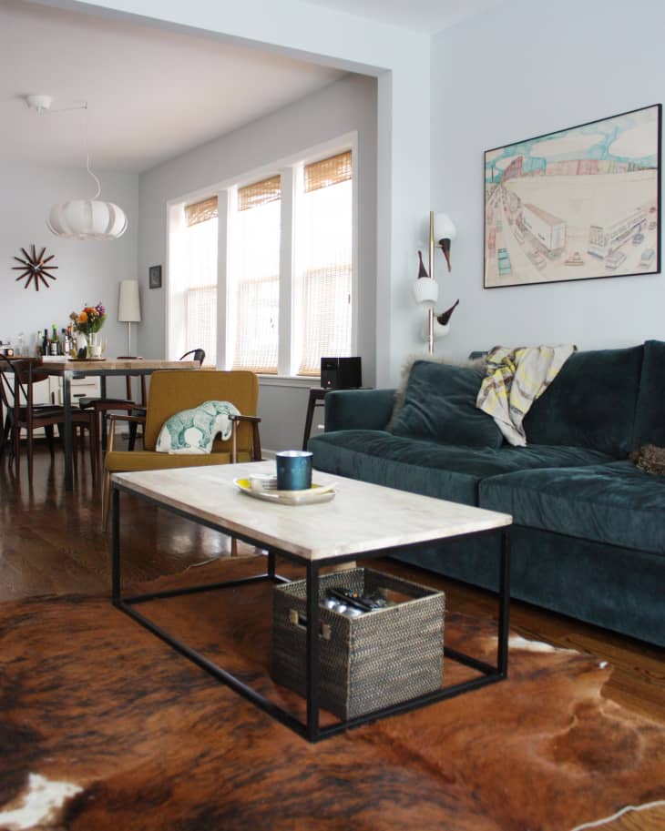 Living room with blue sofa, marble coffee table, cowhide rug, and dining area in the background.