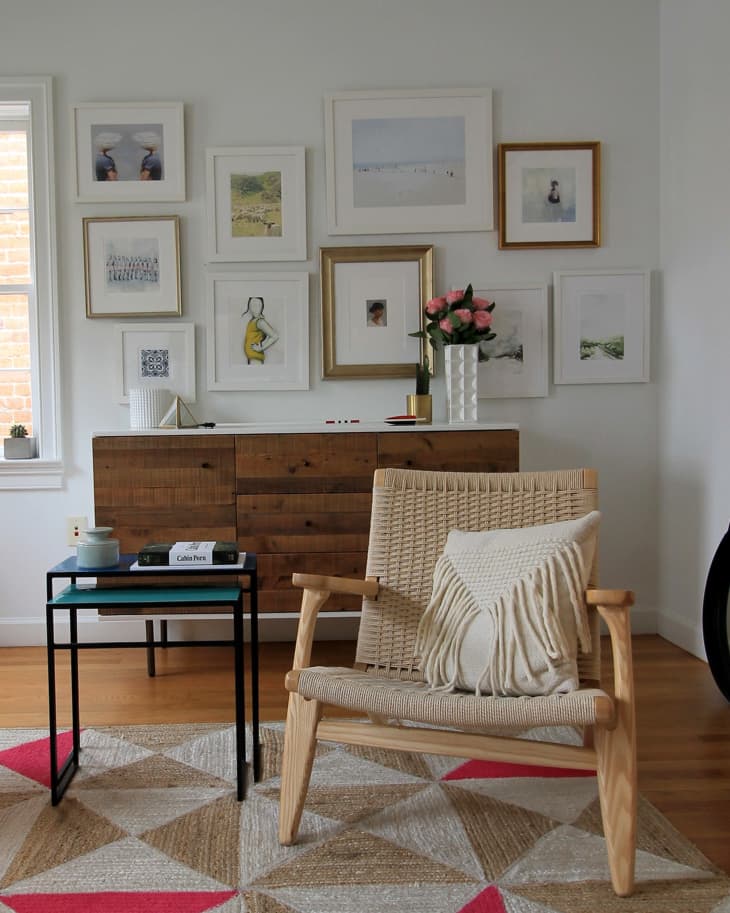 Woven chair with fringed pillow, geometric rug, side table, and gallery wall with framed art in a cozy living room.