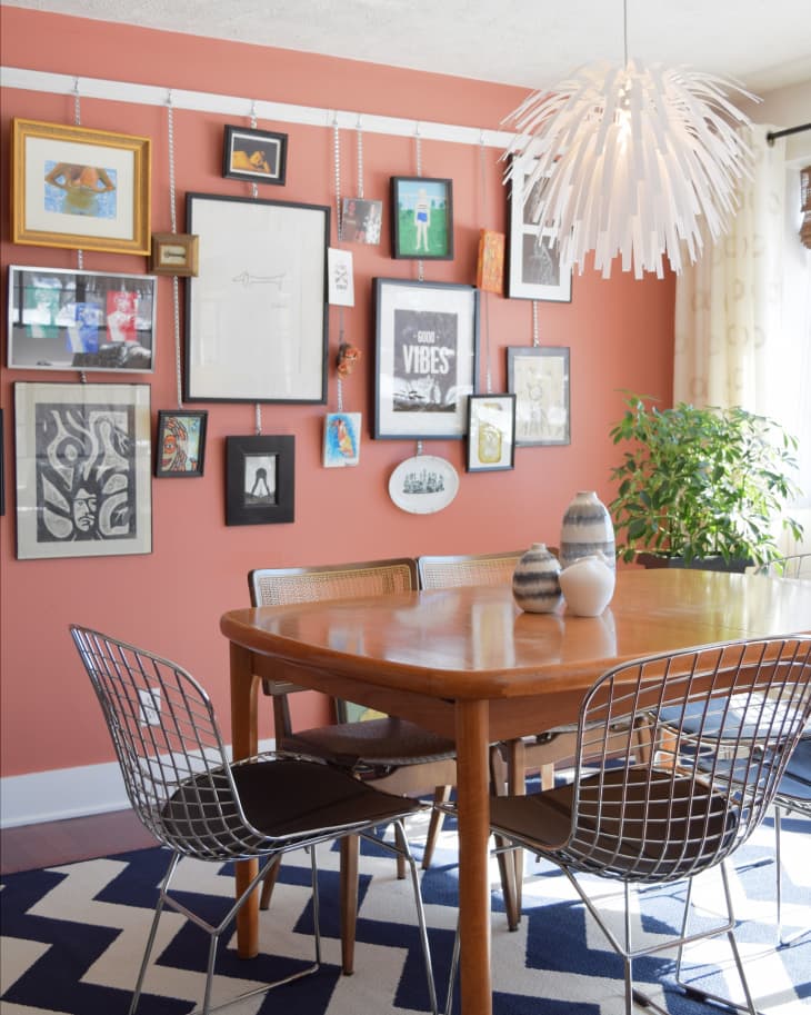 Dining room with a wooden table, wire chairs, zigzag rug, gallery wall, and a white pendant light.