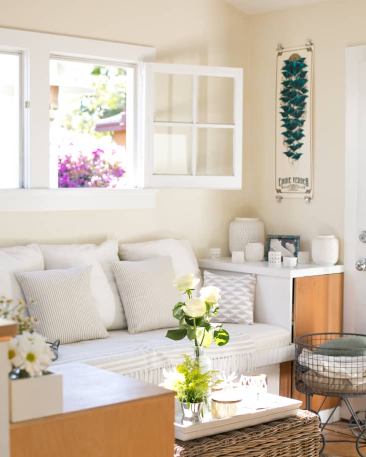 Cozy living room with white sofa, striped pillows, wicker coffee table, and vase of white roses under an open window.
