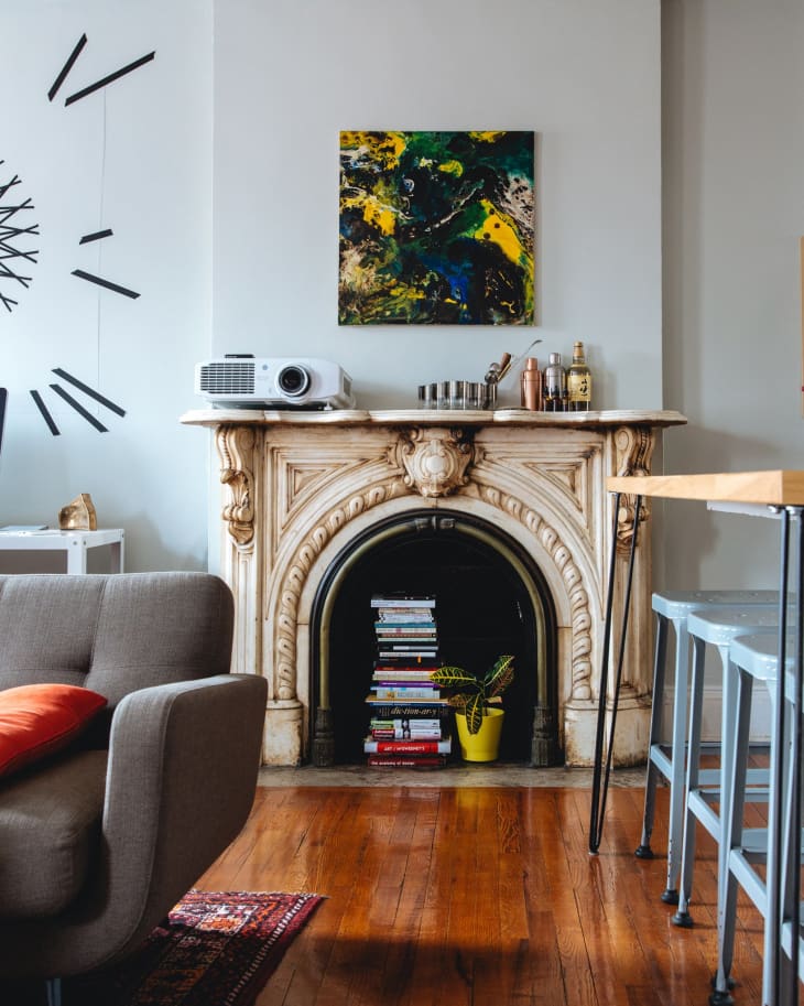 Ornate fireplace with books stacked inside, abstract painting above, and a projector on the mantel.