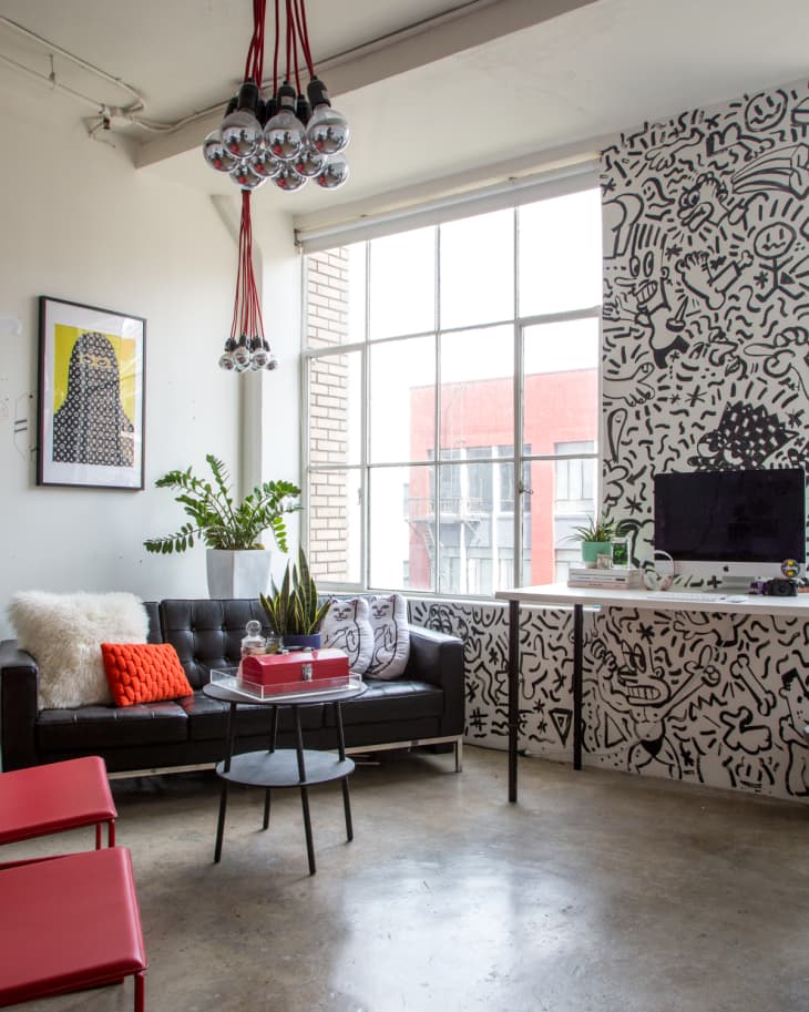 Loft-style living room with black sofa, red accents, abstract wall art, and cluster of hanging light bulbs.