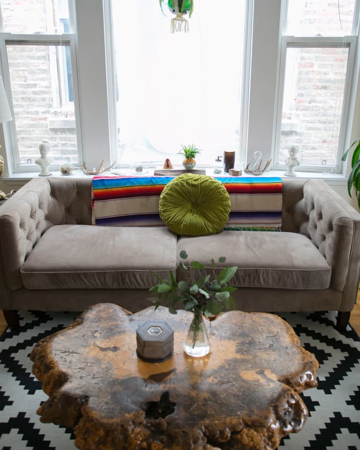 Living room with a beige sofa, colorful striped blanket, green round pillow, rustic wood coffee table, and hanging plant.