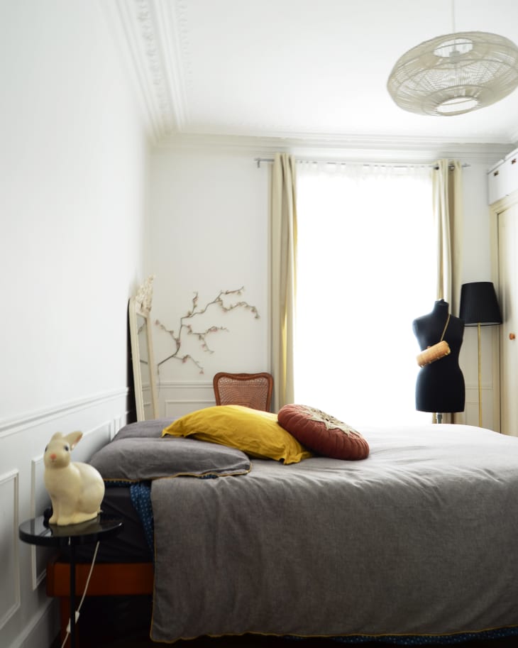 Bedroom with a gray bedspread, yellow and round pillows, a mannequin, and a rabbit lamp on a side table.